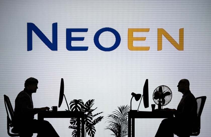 The Neoen logo is seen on an LED screen in the background while two silhouetted people work in an office environment (Editorial use only)