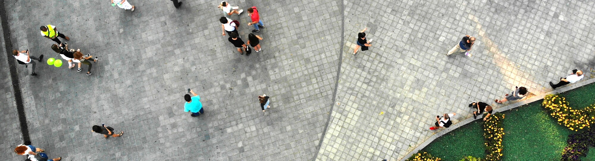 Aerial. People crowd on a city square with flower bed. Top view.