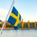 Swedish flag waving over calm waters in the Stockholm archipelago, with Djurgarden island and autumn foliage in the background on a peaceful early Oct