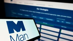 Mobile phone with logo of British financial company Man Group plc on screen in front of business website. Focus on left of phone display.
