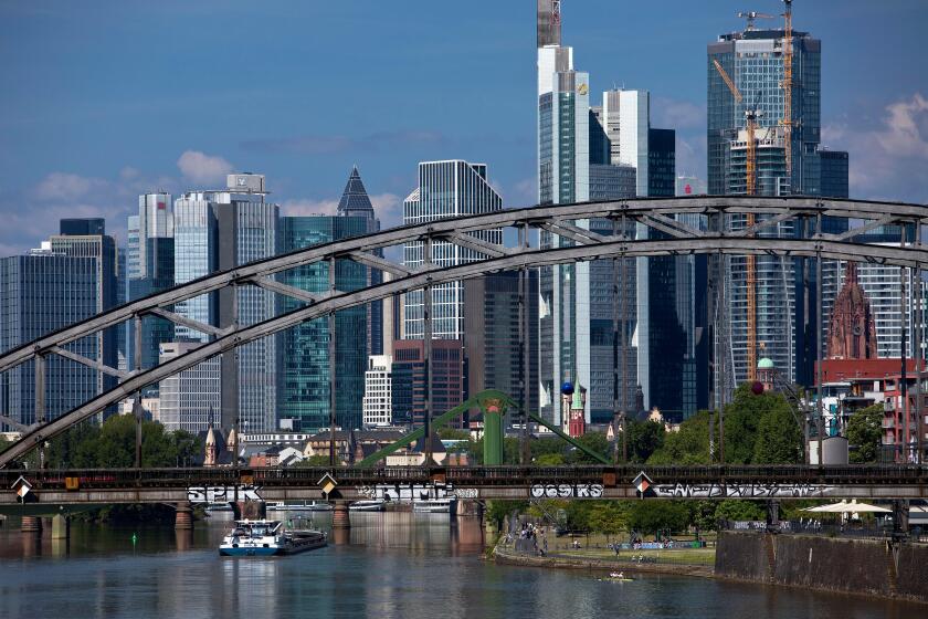 The river Main with the Deutschherrnbruecke bridge and a barge in front of the skyline of Frankfurt am Main, Hesse, Germany