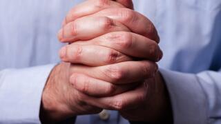 Close up or closeup of hands of faithful mature man praying. Hands folded, interlaced fingers in worship to god. Concept for religion, faith, prayer a