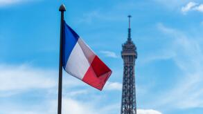 French flag waving against blue sky and Eiffel Tower