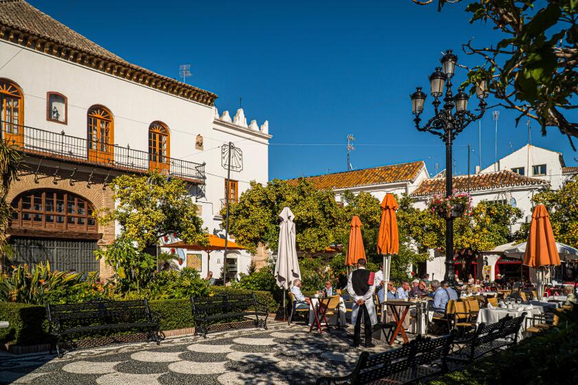 NOVEMBER 21, 2017 - MARBELLA, SPAIN. People having lunch outside in a public plaza on a sunny day. Traditional white buildings.