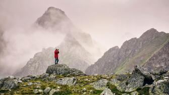 Hiker with camera standing on top of a mountain