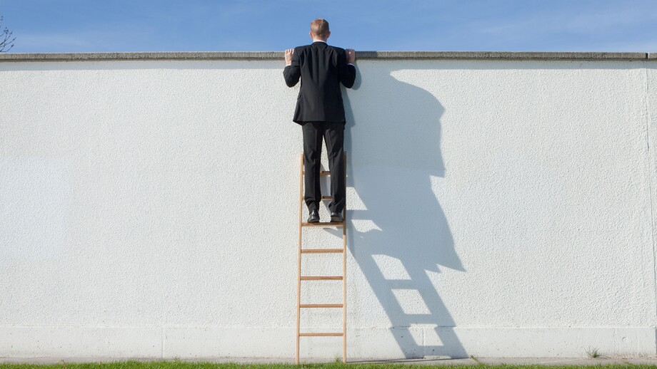 Businessman on ladder looking over wall