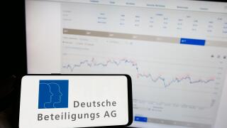 Person holding mobile phone with logo of German company Deutsche Beteiligungs AG (DBAG) on screen in front of web page. Focus on phone display.