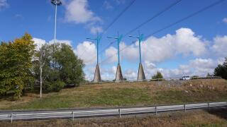 A scenic view of modern transmission towers on a green hill along the road on a sunny day