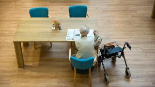 ALMELO, THE NETHERLANDS - JUNE 14, 2016: An elderly woman is reading a newspaper on the table of an elderly home.