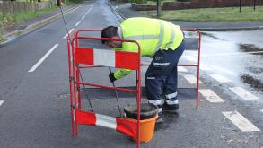 United utilities worker with hi vi jacket digging a hole in the road to locate source of water leak with safety barrier around him