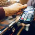 One hand hold machine for cards white another hold dark card for paying money. Men stand at coffee machine