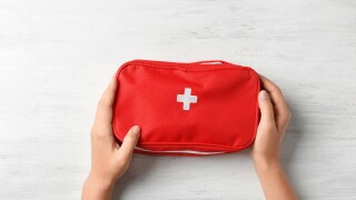 Woman holding first aid kit on wooden background, top view