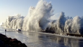 A huge storm surge wave dwarfs a car travelling on Highway 1 at Solimar Beach California