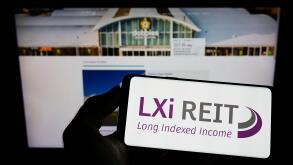Person holding cellphone with logo of British real estate company LXi REIT on screen in front of business webpage. Focus on phone display.