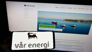Person holding smartphone with logo of Norwegian oil and gas company Var Energi on screen in front of website. Focus on phone display.