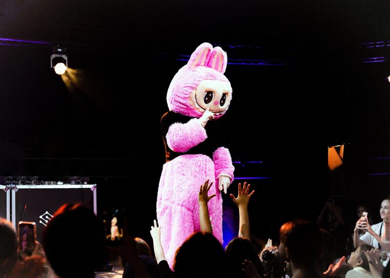 Labubu cheering crowd with bright lights, vivid neon illumination enhances lively performance atmosphere, energetic scene featuring enormous pink