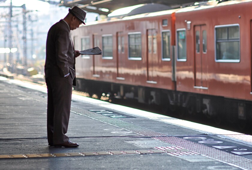 An elderly man reading a newspaper while waiting for a train.