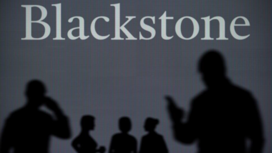 The Blackstone logo is seen on an LED screen in the background while a silhouetted person uses a smartphone in the foreground (Editorial use only)