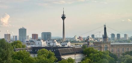 Dusseldorf skyline with Rheinturm tower, modern architecture, and the Rhine under a dramatic cloudy sky.