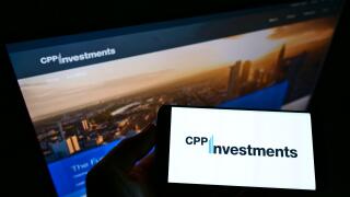 Person holding smartphone with logo of Canada Pension Plan Investment Board (CPPIB) on screen in front of website. Focus on phone display.