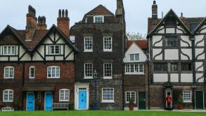 A picture of a few old rural british houses with blue door and with a beefeater guard in front of one of them.