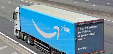 Aerial side & back view of white lorry truck blue Amazon supply chain articulated delivery trailer with advertising on rear door travel on UK motorway