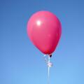 A single pink balloon against the blue sky in closeup