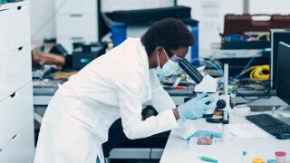 Scientist african american black woman in face mask and gloves working in laboratory with electronic tech instruments and microscope.