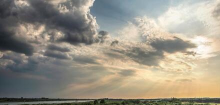 Dramatic skies with low sun and dark clouds approaching over the island of IJsselmonde and the Oude Maas river as seen from the artificial hill at Car