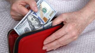 Elderly woman takes out US dollars from her wallet. Concept of pension payments, savings at retirement, pensioner with money