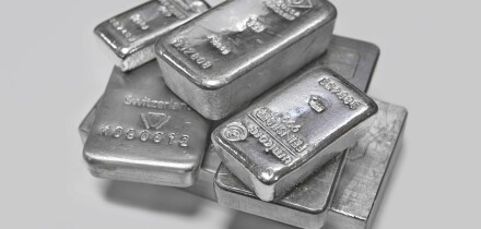 Silver bullion bars in a pile on plain grey background
