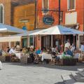Restaurant piazza Italy, view in summer of a group of people dining outside a pizzeria in the scenic port of Chioggia, Comune of Venice, Italy
