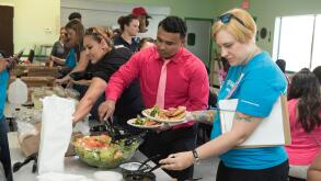 Adult volunteers serve themselves salad in cafeteria during after-school activity at middle school in Austin, Texas