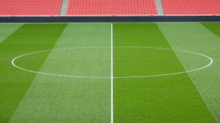 centre circle of a football pitch and bright red seating inside an empty football stadium.