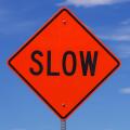 orange slow road sign with black letters in front of the sky