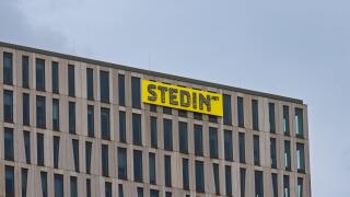 The top corner of the modern Stedin office building, showing its distinctive facade and the company's bright yellow logo against a grey sky. Rotterdam