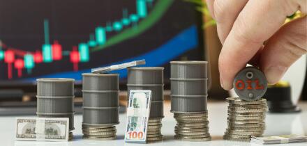 Hand Stacking Oil Barrel on Coins with Cash and Trading Chart
