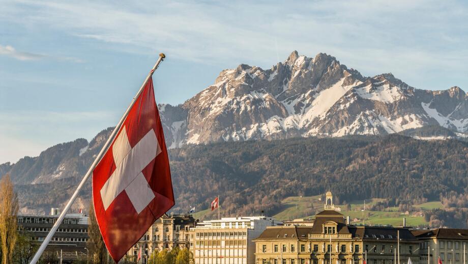 Swiss National Flag in Lucerne in Central Switzerland with the mountain range of Mt Pilatus in the background