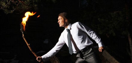 Image of brave man with burning stick in darkness