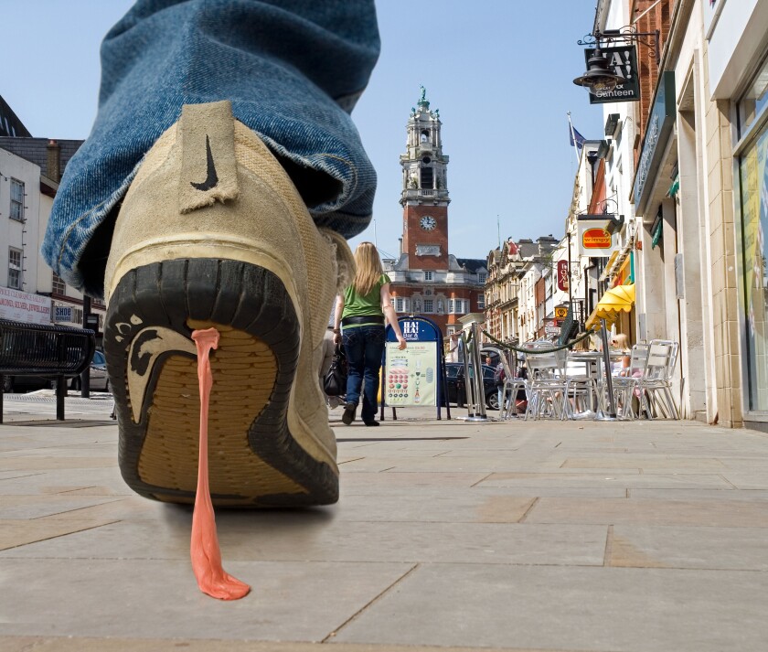 Close up of Bubble gum stuck to trainers. A pedestrian walking along a street gets discarded  gum stuck to his trainers