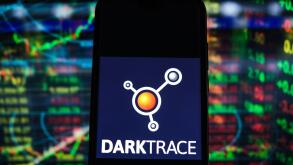 In this photo illustration a Darktrace logo seen displayed on a smartphone with stock market percentages in the background.