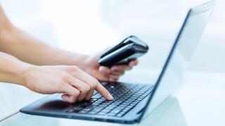 Online banking, shopping and booking. Closeup of a person's hand holding a wallet while using a laptop computer.