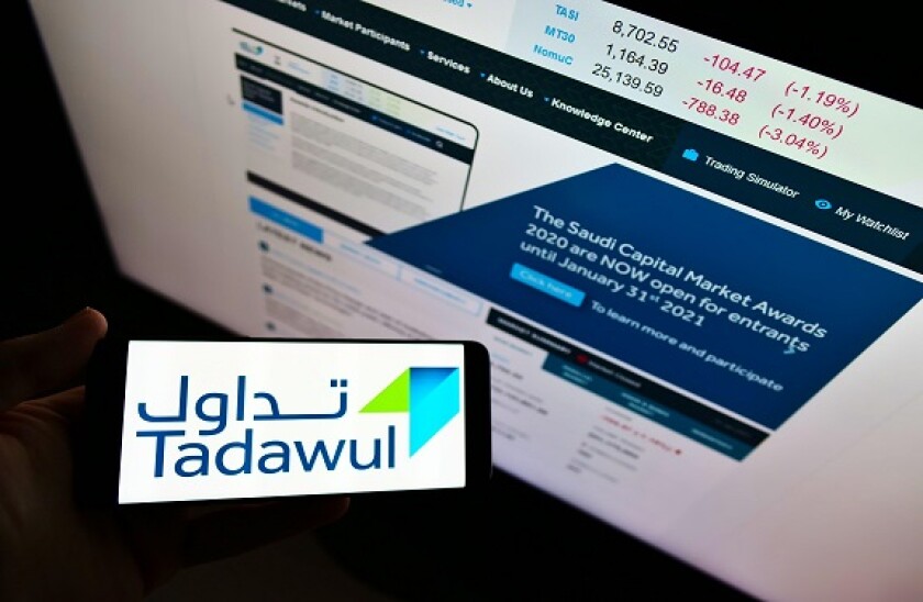 Person holding smartphone with business logo of Saudi Arabian stock exchange Tadawul on screen in front of website. Focus on phone display.