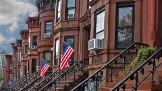 Brownstone row houses in Brooklyn neighborhood with US flags and cloudy sky
