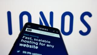 Smartphone with website of German web hosting company Ionos SE on screen in front of business logo. Focus on top-left of phone display.