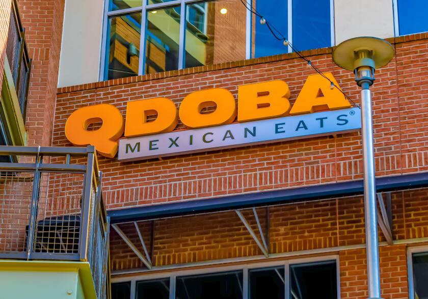 Qdoba Mexican Eats restaurant's exterior facade brand and logo signage in orange letters on red brick below reflective windows with lamppost.
