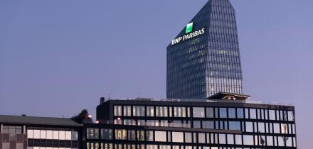 Glass building headquarters of the French bank BNP Paribas with the logo sign illuminated at sunset. Milan, Italy.