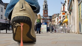 Close up of Bubble gum stuck to trainers. A pedestrian walking along a street gets discarded  gum stuck to his trainers