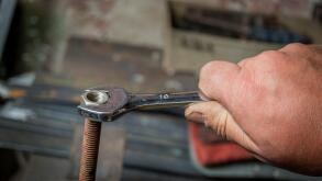 worker hand tightening or loosening a nut of a rusty bolt with a wrench on white background