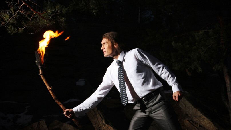 Image of brave man with burning stick in darkness
